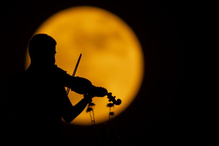 A person plays the violin as the full moon appears over Halabja, Iraq on June 10, 2025.