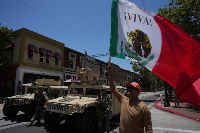 A protester waves a flag standing by California National Guard parked along a street in Santa Ana, Calif. on Tuesday, June 10, 2025.