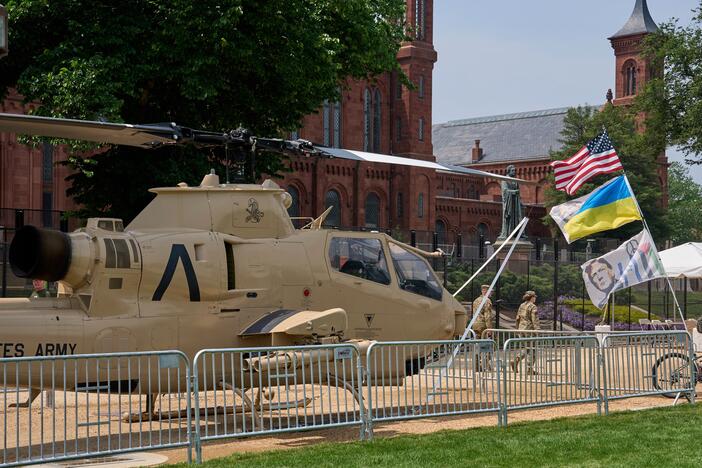 A man bicycles with several flags past a helicopter on display during preparations for an upcoming military parade commemorating the Army's 250th anniversary and coinciding with President Donald Trump's 79th birthday.