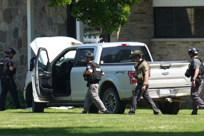 Police walk by an idle vehicle near CrossPointe Community Church in Wayne, Mich., Sunday, June 23, 2025.