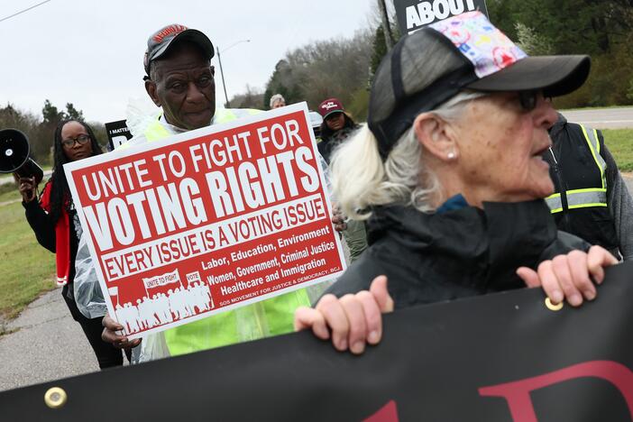 Demonstrators walk in Selma, Ala., in March with a sign saying "UNITE TO FIGHT FOR VOTING RIGHTS" to commemorate the 60th anniversary of the Bloody Sunday march that galvanized the passage of the Voting Rights Act of 1965.