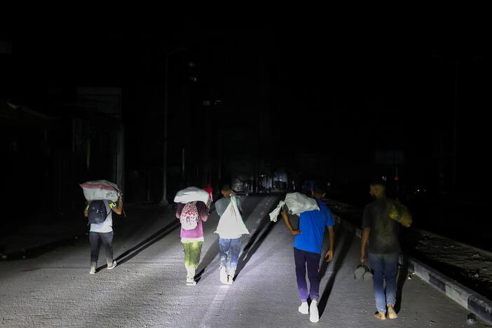 Palestinians walk back, carrying parcels collected from a food aid distribution point set up by the privately run Gaza Humanitarian Foundation (GHF) on the Salaheddin road, at the Nuseirat refugee camp in the central Gaza Strip on June 24, 2025.