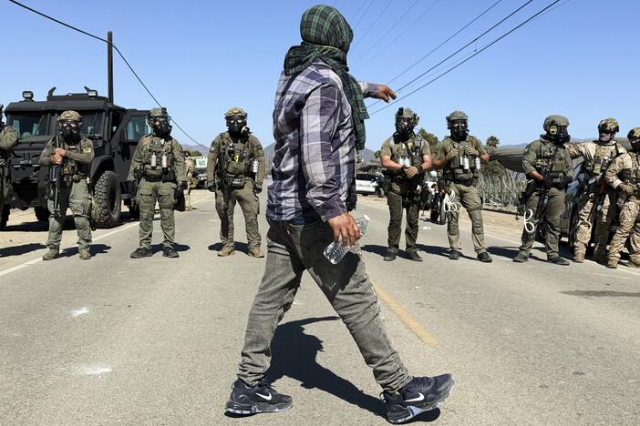 A demonstrator walks in front of federal agents blocking a road during an immigration raid in Camarillo, Calif., Thursday, July 10, 2025.