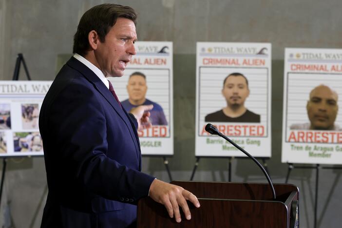 Florida Gov. Ron DeSantis speaks during a press conference, in front of posters of people that law enforcement arrested. DeSantis talked about a multi-agency immigration enforcement effort named Operation Tidal Wave that they say resulted in more than 1,100 arrests in a single week in Florida.
