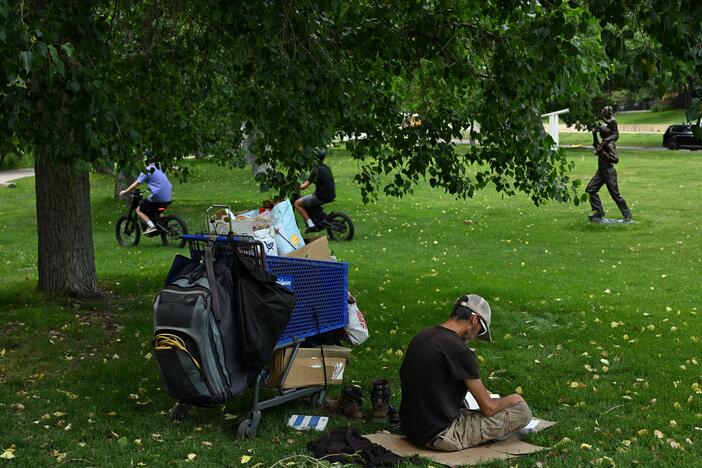 A man who identifies as homeless reads a book under the shade of a tree during high 90-degree temperatures last month in Boulder, Colo.