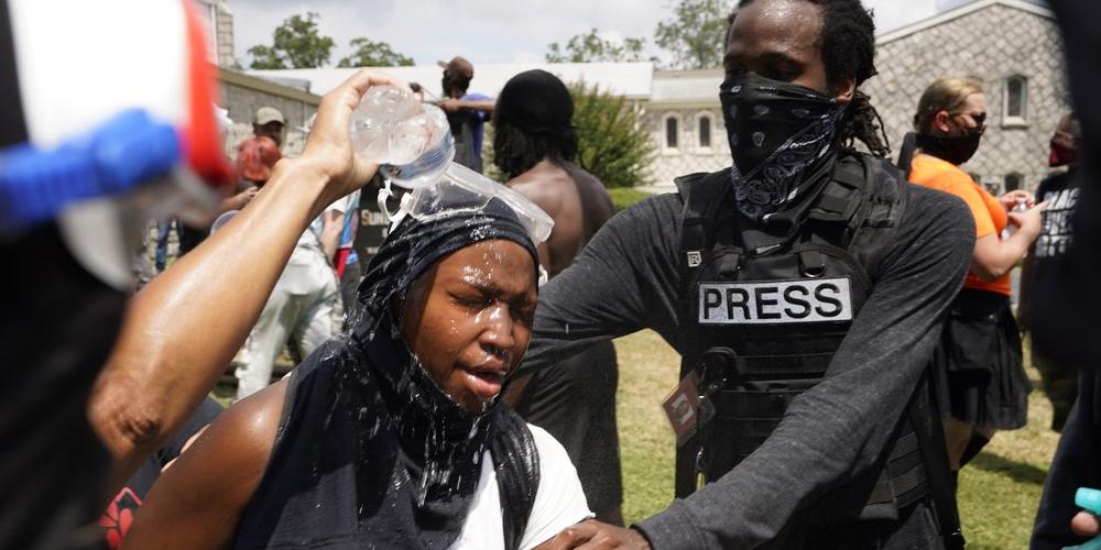 A woman is helped after being sprayed with an unknown agent during a protest , Saturday, Aug. 15, 2020, in Stone Mountain Village, Ga. Several dozen people waving Confederate flags, many of them wearing military gear, gathered in downtown Stone Mountain where they faced off against a few hundred counterprotesters, many of whom wore shirts or carried signs expressing support for the Black Lives Matter movement. 