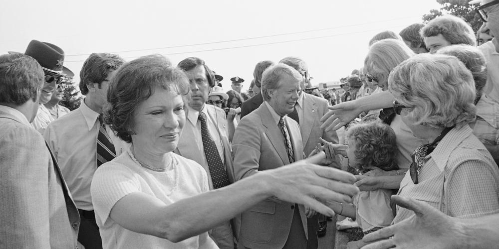 Rosalynn Carter walks ahead of her husband, Democratic presidential candidate Jimmy Carter, shaking hands with persons greeting them on arrival in Asheville, N.C., May 2, 1976, where they attended a $1,000 a plate fundraising dinner.