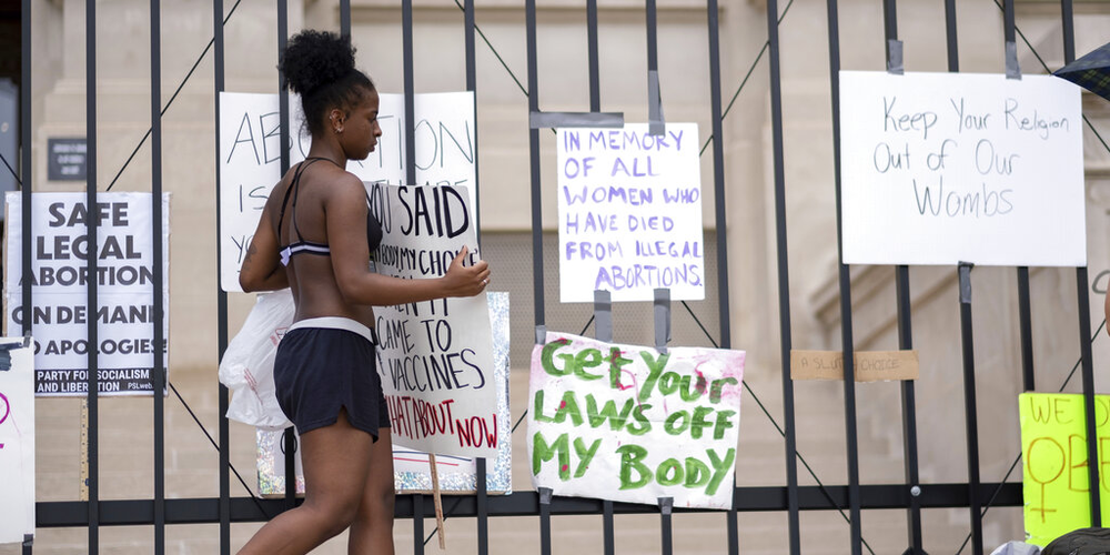 Nea Walker hangs a sign on the fence in front of the Georgia State Capitol while protesting the overturning of Roe v. Wade on Sunday, June 26, 2022. 