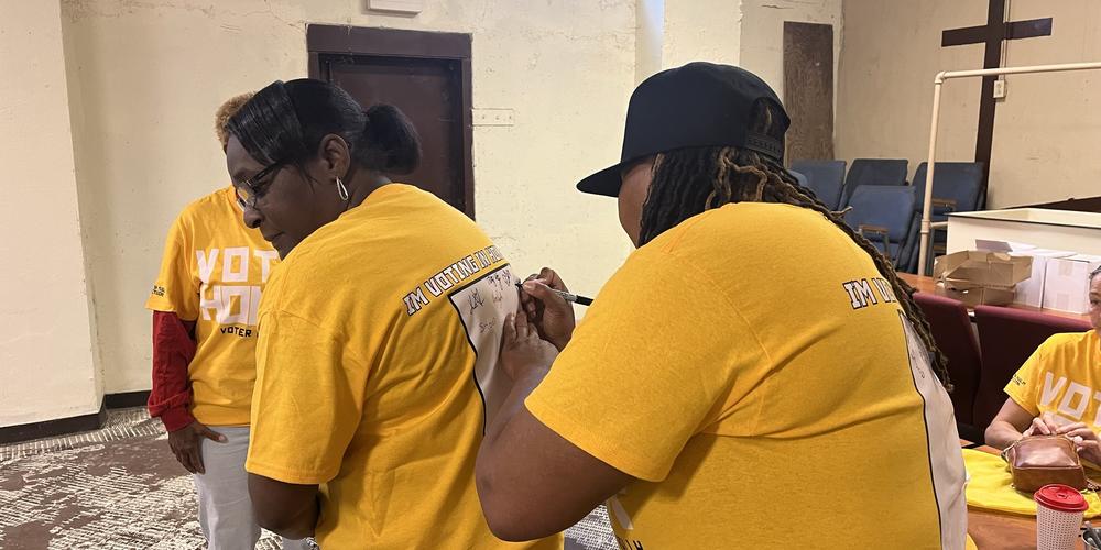 Ikethia Daniels signs the back of another canvassers shirt asking people to vote in her honor.