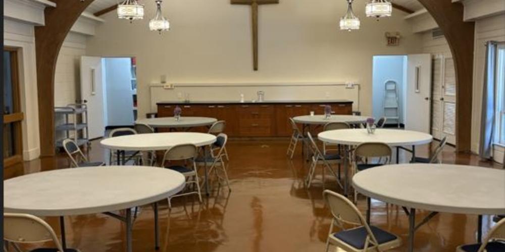 The dining room with tables and a giant cross on the back wall