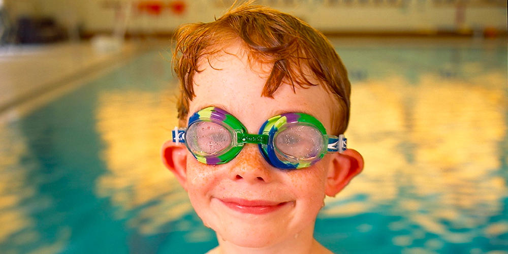 Young boy swimmer wearing goggles. Photography by Billy Howard