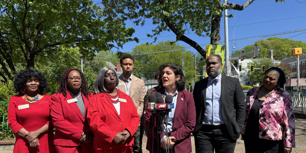 From left to right: State Reps. Viola Davis, Kim Schofield, Sandra Scott, Eric Bell, Atlanta city councilwoman Liliana Bakhtiari, Atlanta NAACP President Gerald Griggs, and state Sen. Gail Davenport present at the press conference at the site of the crash to call for an end to high speed chases. Credit: Sarah Kallis/GPB News