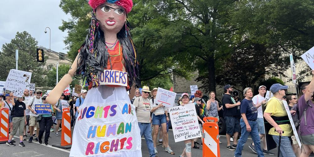 A giant paper mache woman wearing a sign saying workers rights are human rights.