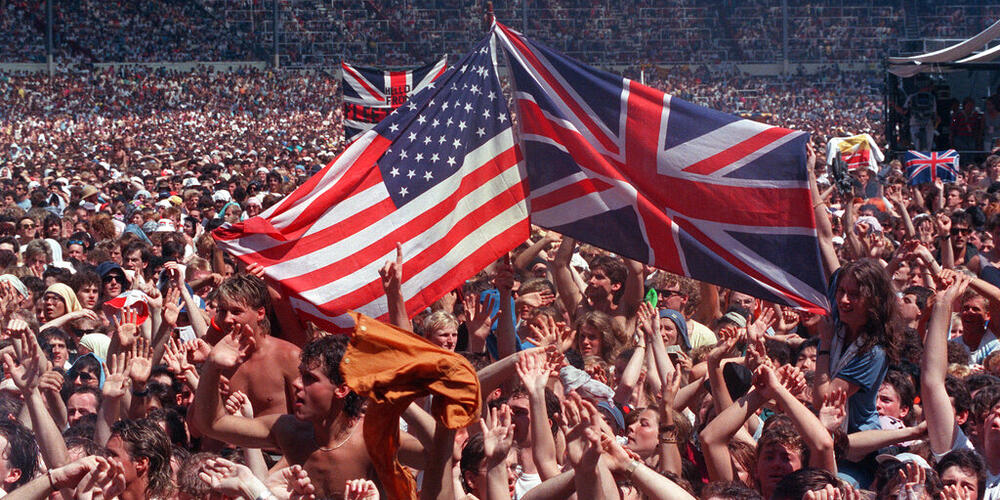 Fans wave flags, the U.S. Stars and Stripes and Britain's Union Jack, at Wembley Stadium, London, July 13, 1985, at the end of the Live Aid famine relief concert for Africa. (AP Photo/Joe Schaber)