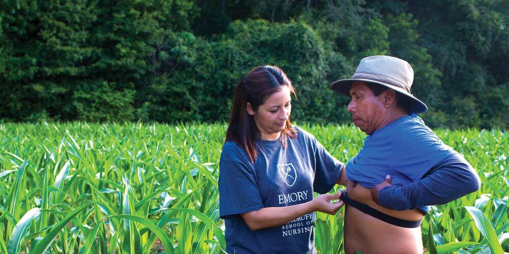 Roxana Chicas places a heat monitor on a a farmworker's chest in a green field in Oxford, Georgia. (Kay Hinton / Emory University)