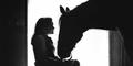 Silhouetted woman in wheelchair greeting a horse. Photography by Billy Howard