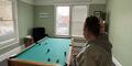 A woman in a gray hooded jacket playing pool by herself at Living Proof Recovery in Rome, Ga.